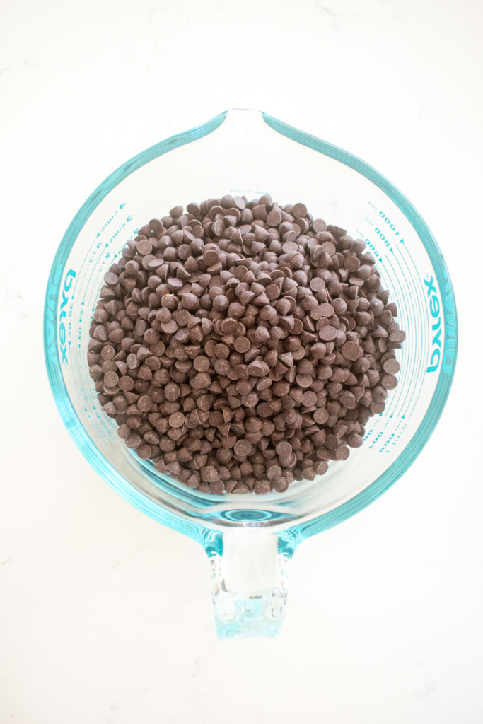 mini dark chocolate chips in a pyrex measuring cup on a white marble counter.