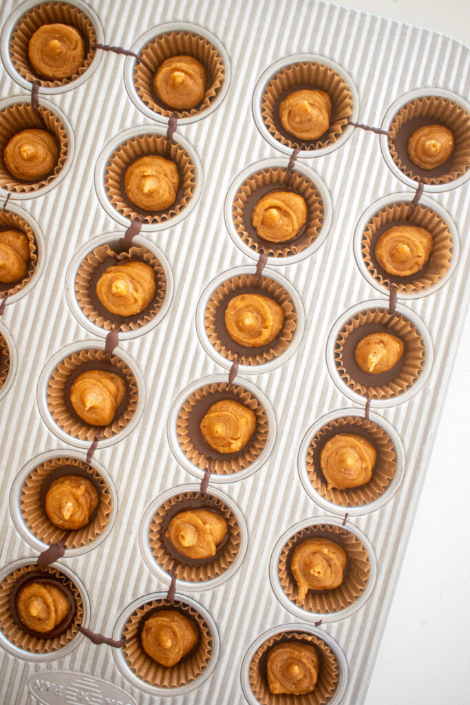 vegan dark chocolate mini peanut butter cups being filled in a mini muffin pan on a white marble counter.