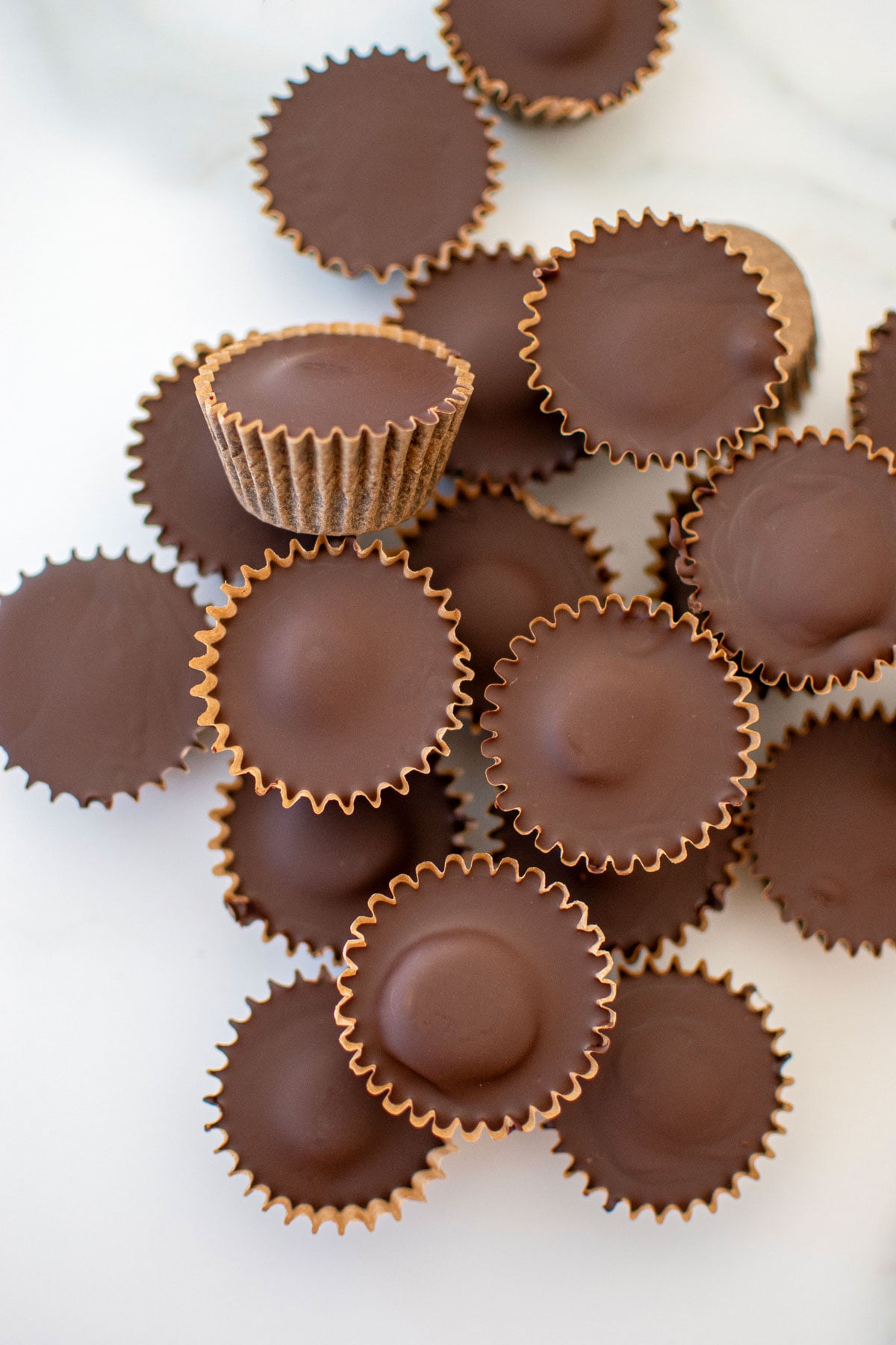 pile of vegan dark chocolate mini peanut butter cups on a white marble counter.
