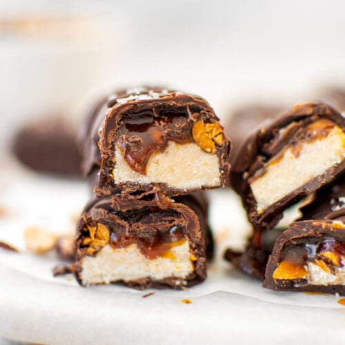 vegan snickers bar cut in half stacked on top of each other on a marble board with caramel dripping out.