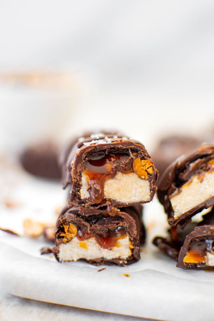 vegan snickers bar cut in half stacked on top of each other on a marble board with caramel dripping out.