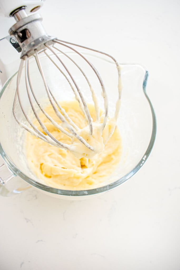 creamy bone broth mashed potatoes in a glass mixing bowl with a whisk on a marble counter.