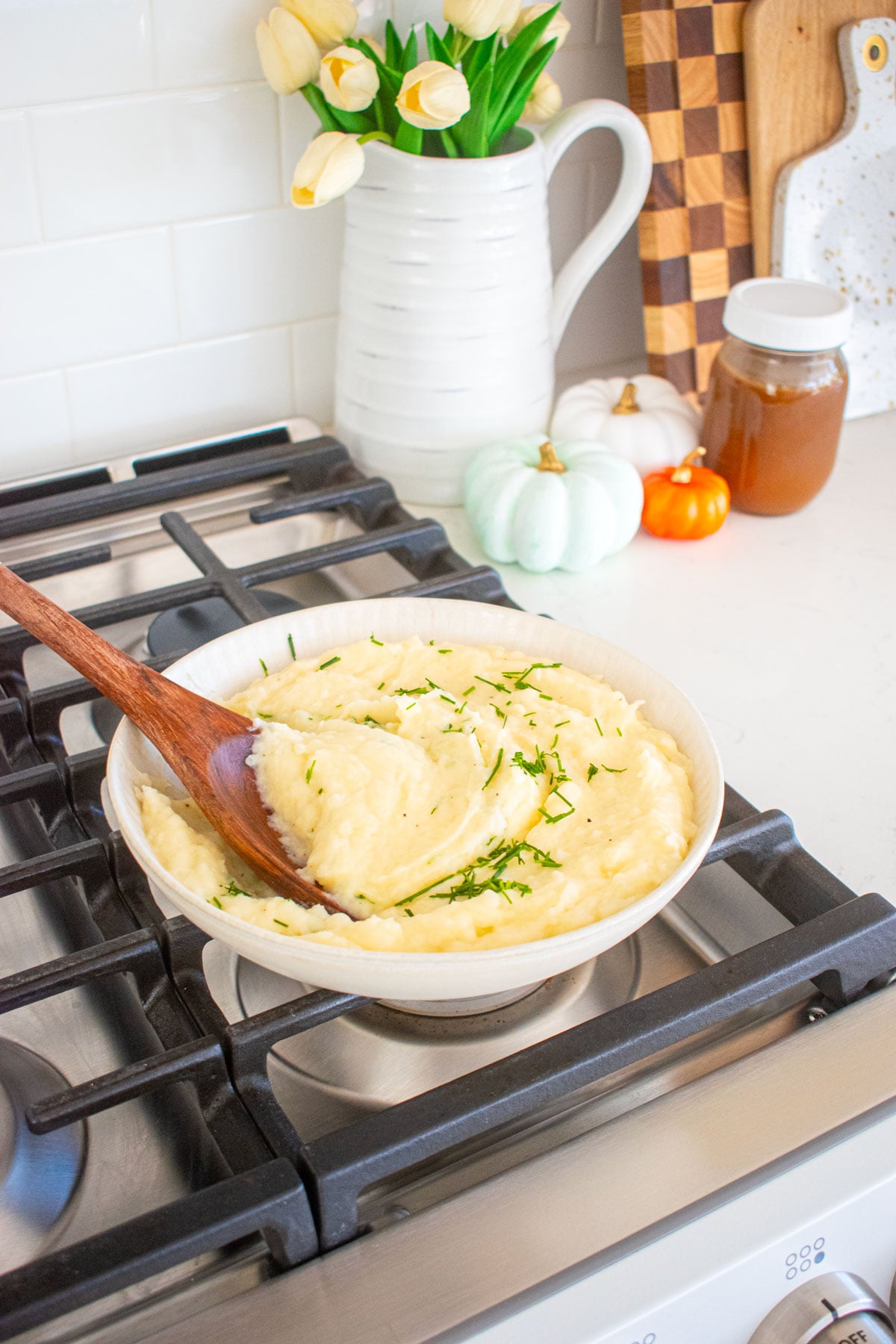 bowl of bone broth mashed potatoes with fresh chives sitting on top of an oven with a serving spoon in them.