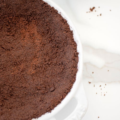 chocolate graham cracker crust in a white pie dish on a white marble countertop.