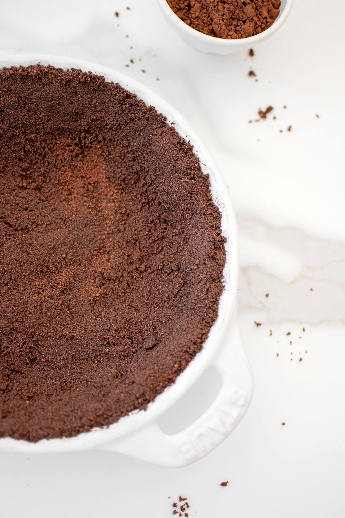 chocolate graham cracker crust in a white pie dish on a white marble countertop.