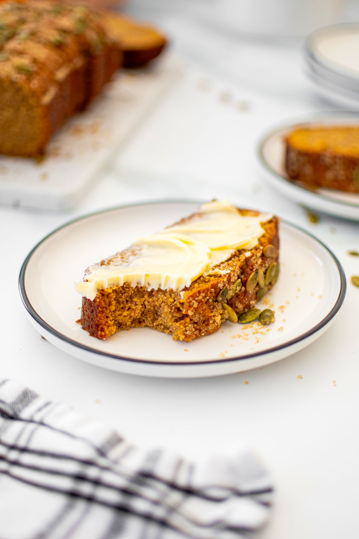 slice of cinnamon sweet potato bread with butter with a bite taken out on a white plate on a marble counter.