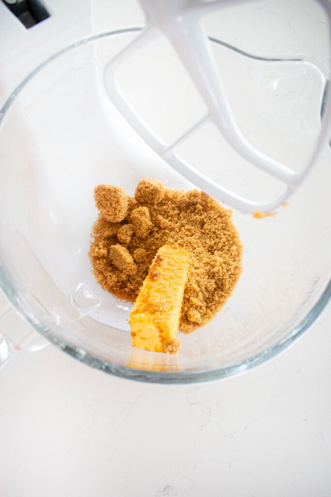 butter and light brown sugar in a glass mixing bowl on a white marble counter.