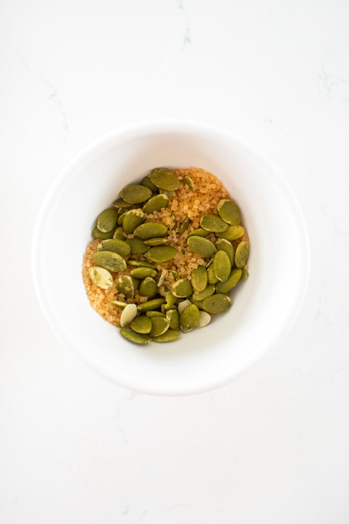 pumpkin seeds and turbinado sugar in a small bowl on a white marble counter.