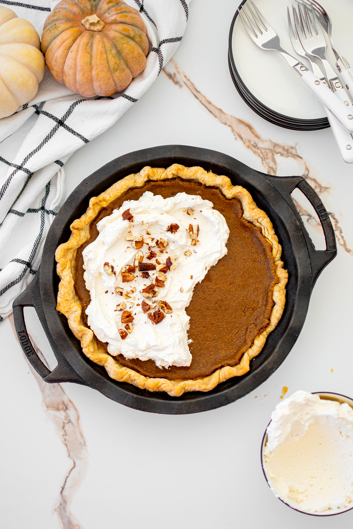 eggless sourdough pumpkin pie with whipped cream in a cast iron pie pan on a white marble counter.