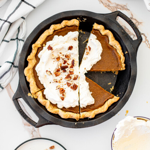 eggless sourdough pumpkin pie with whipped cream in a cast iron pie pan on a white marble counter.