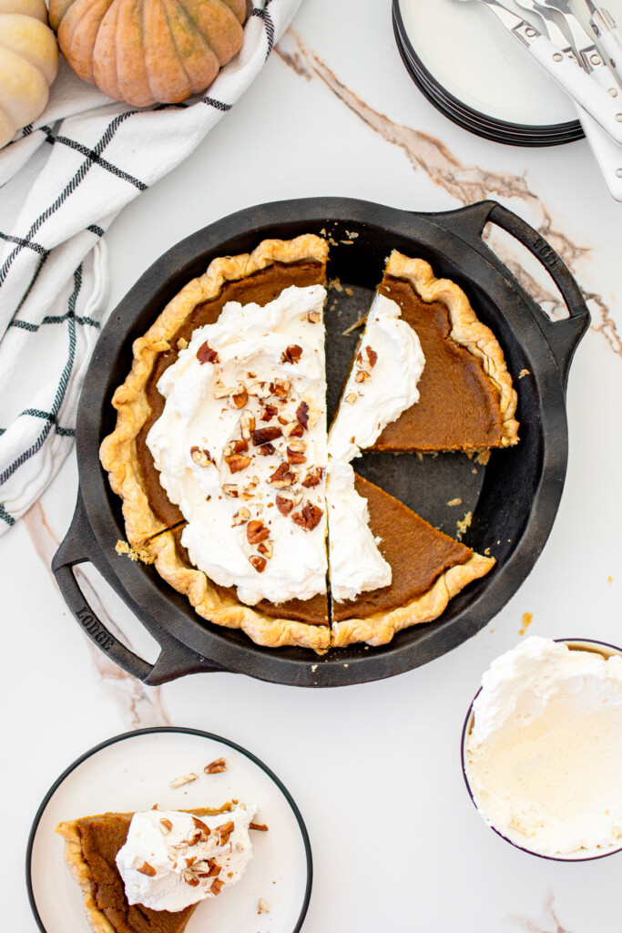 eggless sourdough pumpkin pie with whipped cream in a cast iron pie pan on a white marble counter.