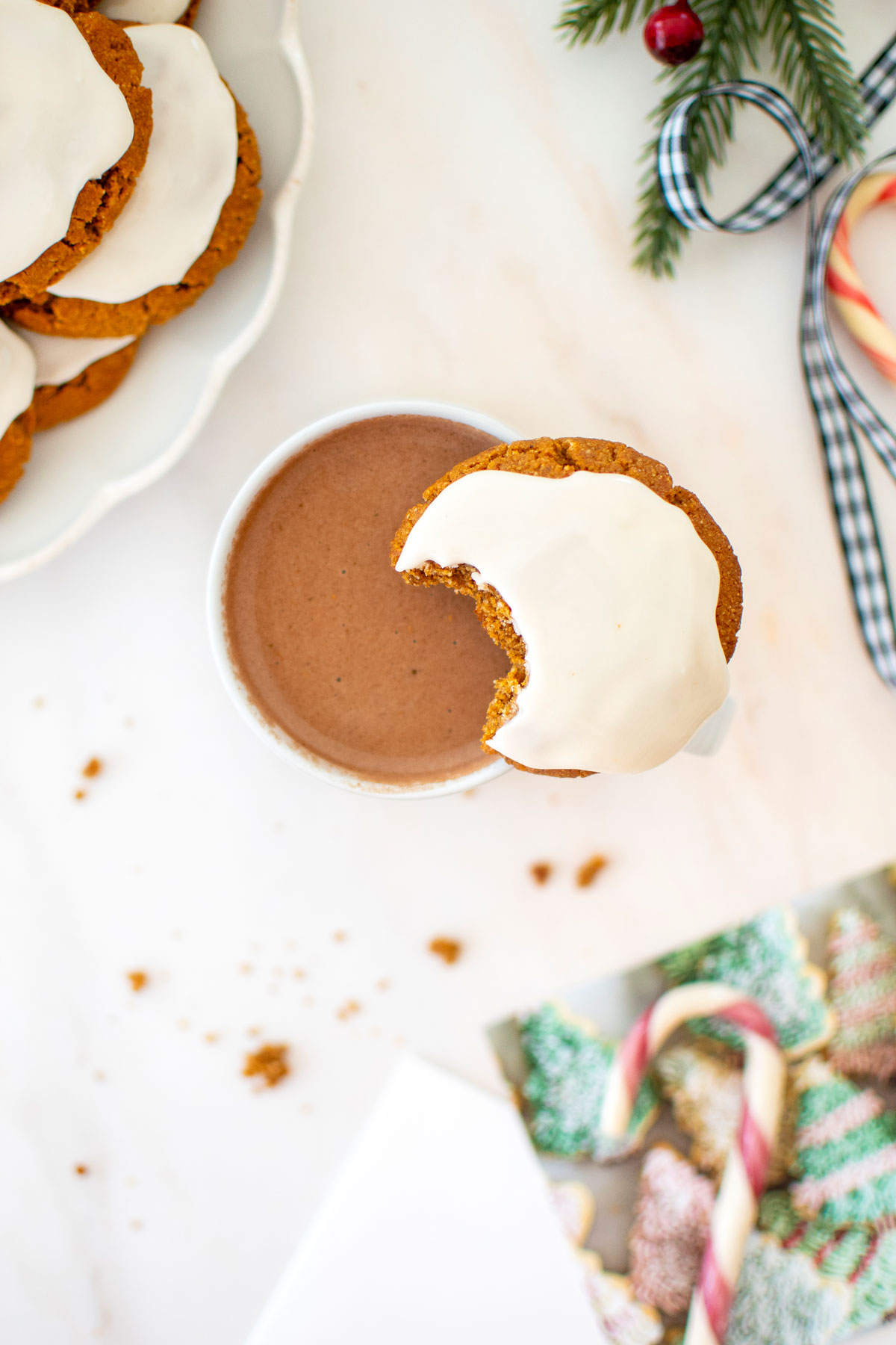 gluten free frosted gingerbread cookie with a bite taken out sitting on top of a mug of hot cocoa on a marble counter.
