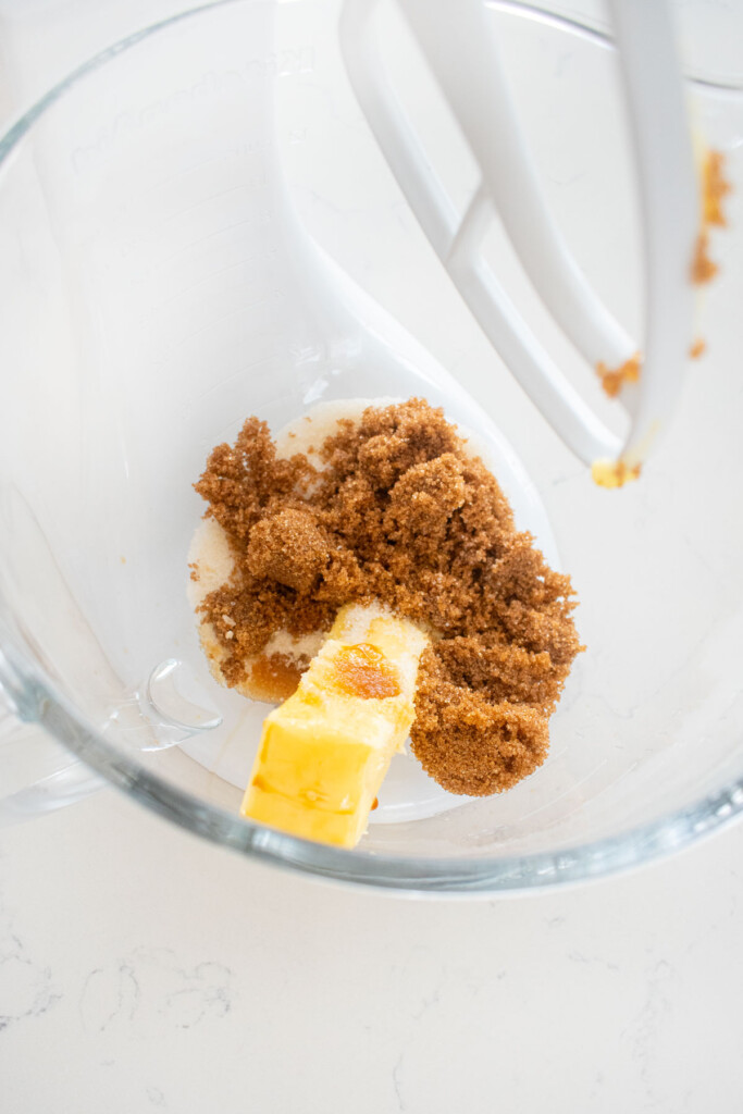 butter, dark brown sugar and cane sugar in a glass mixing bowl on a white marble counter.