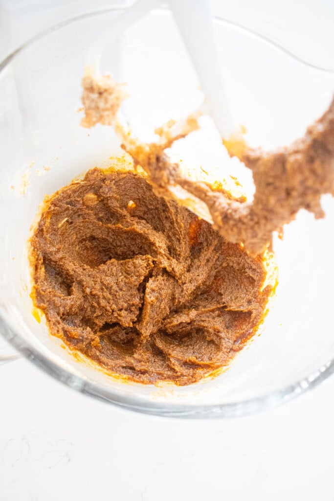 creamed butter, sugar and molasses in a glass mixing bowl on a white marble counter.