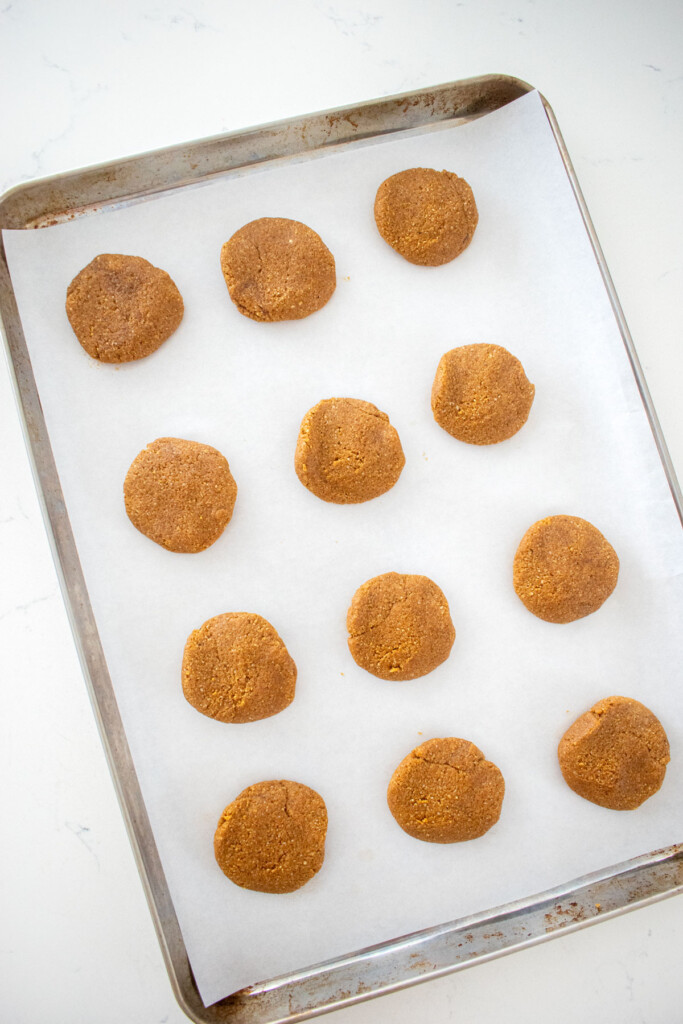 gluten free gingerbread cookie dough balls on a baking sheet on a white marble counter.