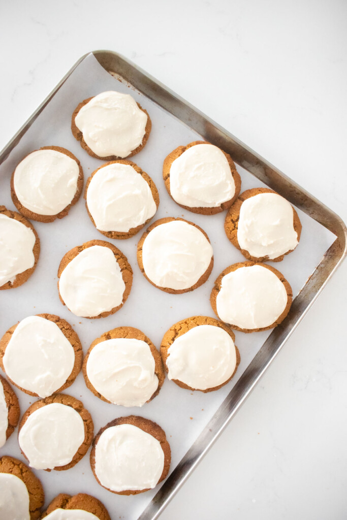 gluten free frosted gingerbread cookies on a baking sheet on a white marble counter.