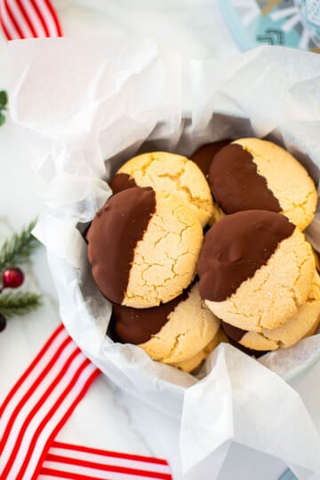 cookie tin of gluten free chocolate peppermint shortbread cookies on a marble counter with red holiday ribbon and holly.