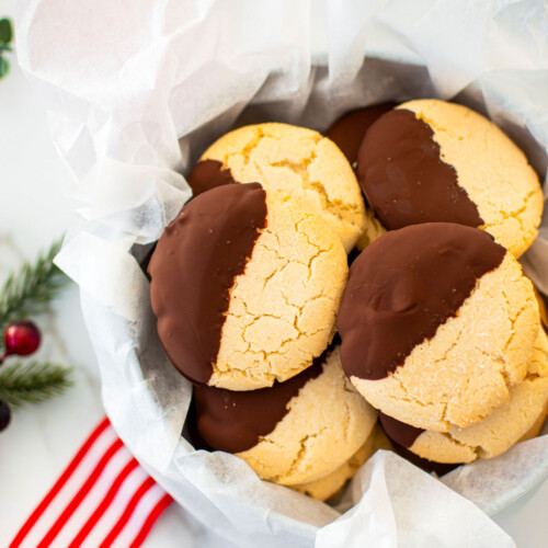 cookie tin of gluten free chocolate peppermint shortbread cookies on a marble counter with red holiday ribbon and holly.