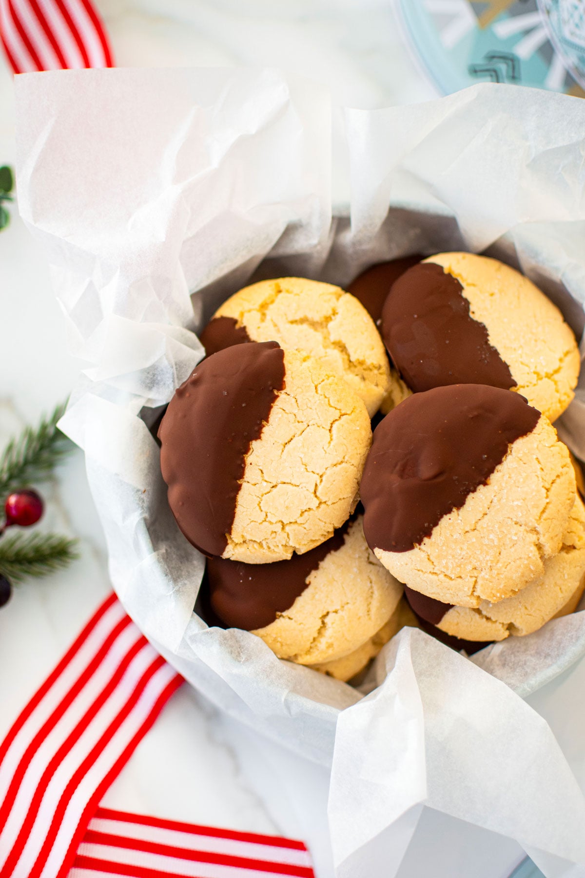 cookie tin of gluten free chocolate peppermint shortbread cookies on a marble counter with red holiday ribbon and holly.