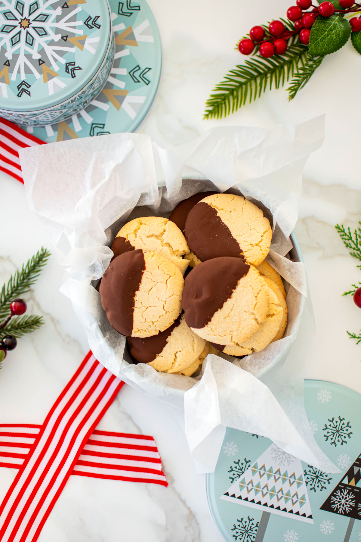 cookie tin of gluten free chocolate peppermint shortbread cookies on a marble counter with red holiday ribbon and holly.