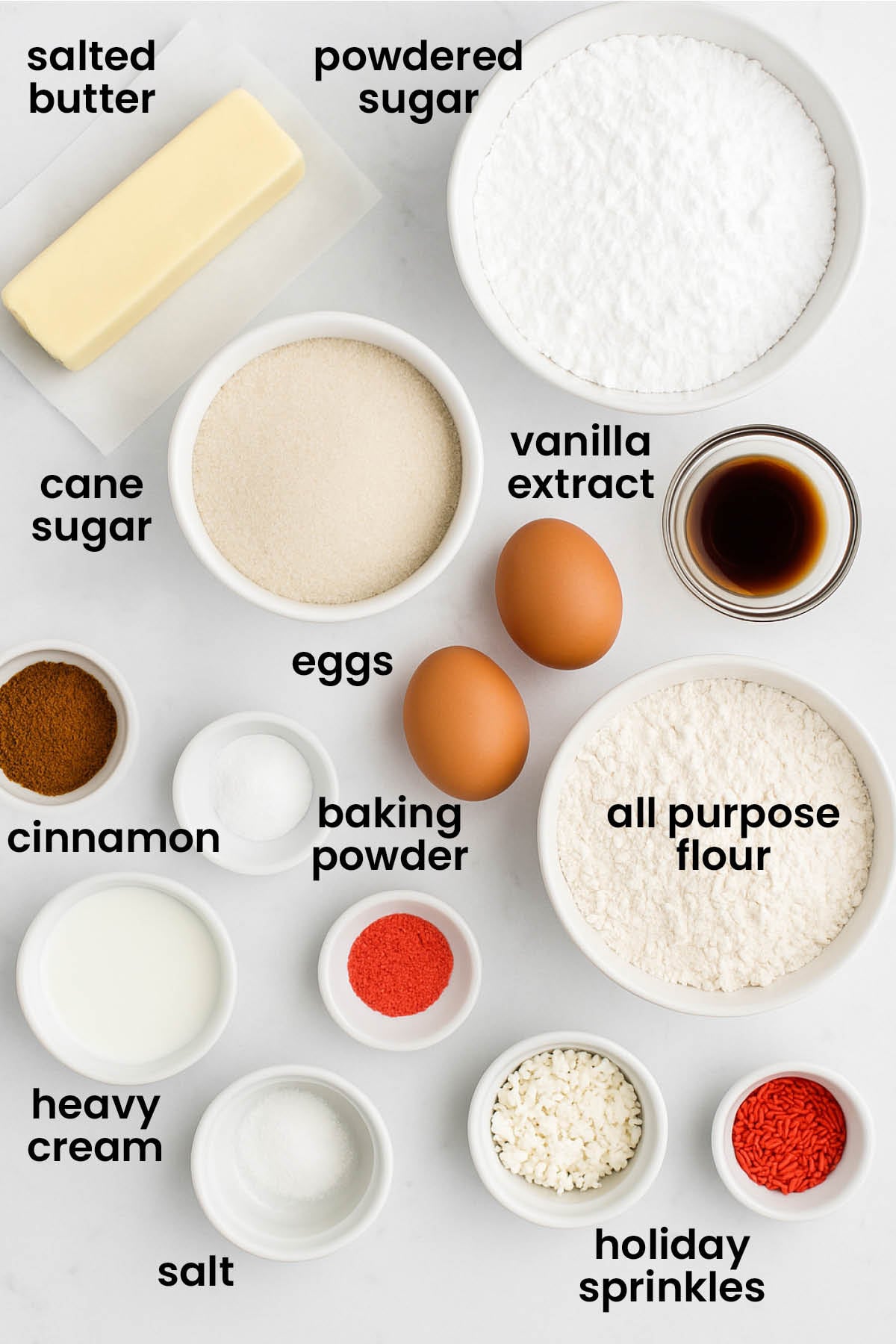 individual ingredients for holiday sugar cookies with icing laid out against a white background.