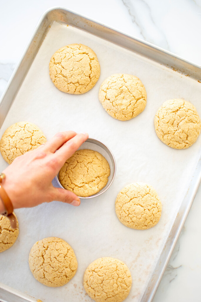 woman swirling cookies with a cookie cutter to round them out on a baking sheet.
