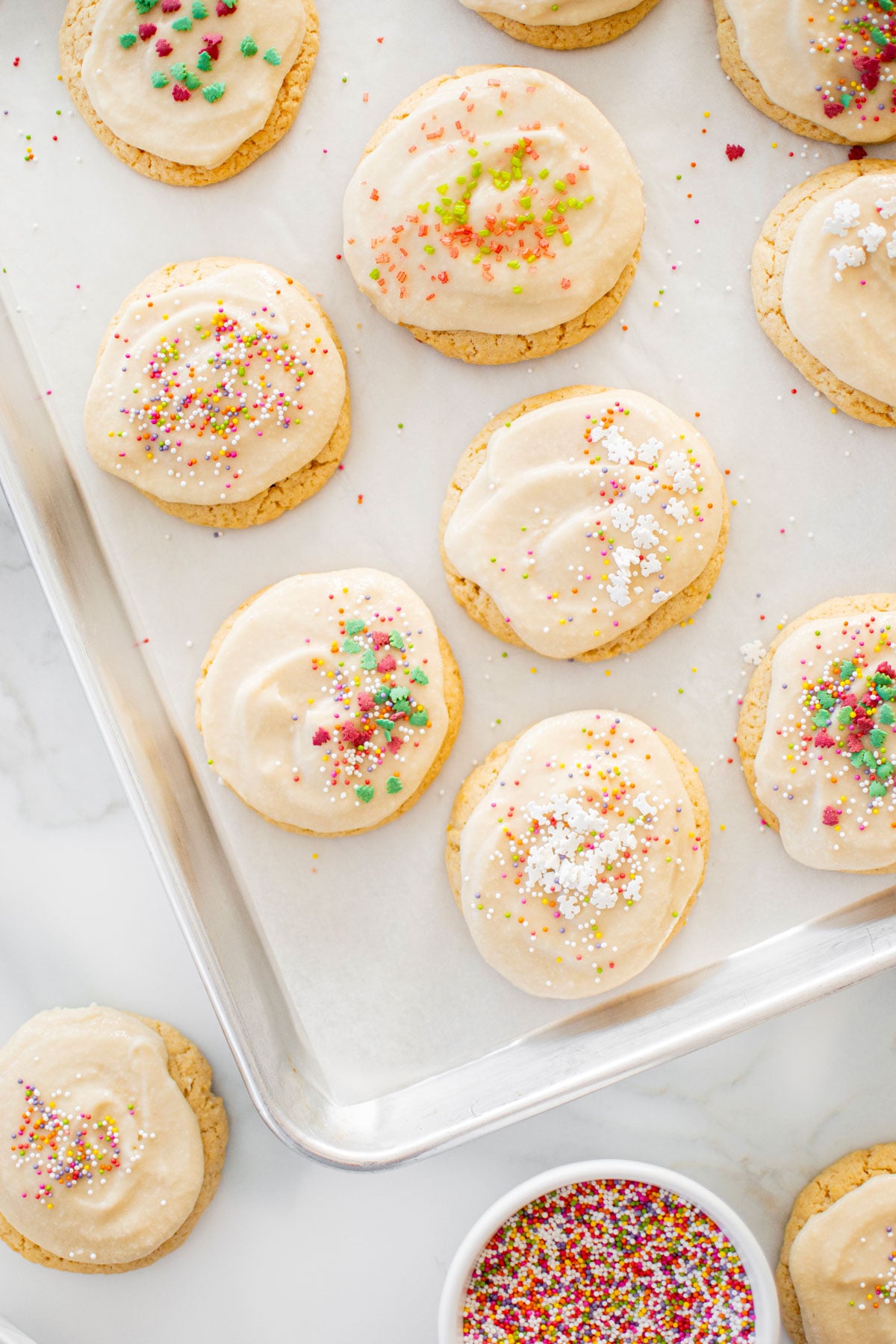 holiday sugar cookies with icing and holiday sprinkles on a baking sheet.