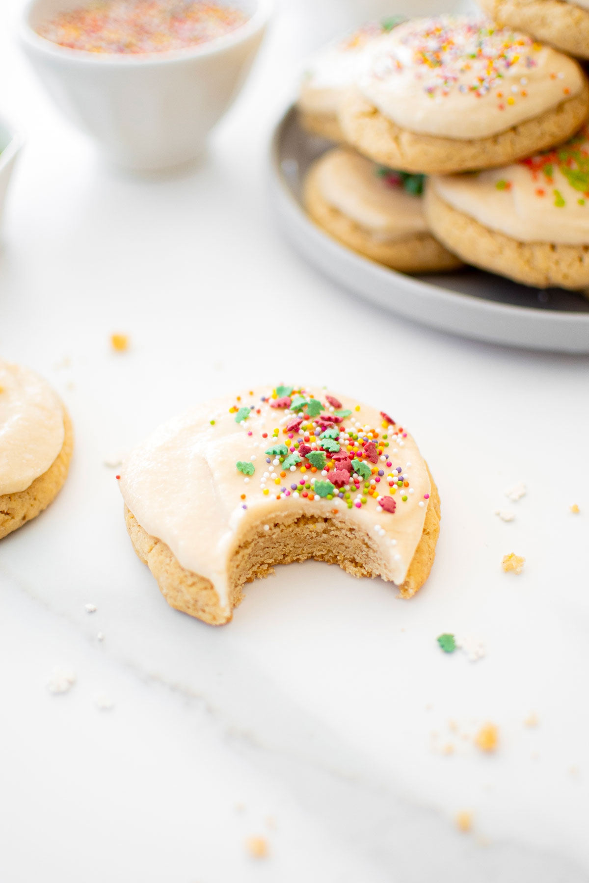 sugar cookie with icing and holiday sprinkles with a bite taken out on a white marble counter.