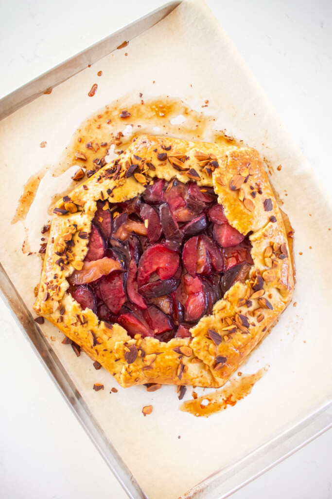 baked honey almond plum galette on a baking sheet with golden brown crust and toasted almonds on the crust.
