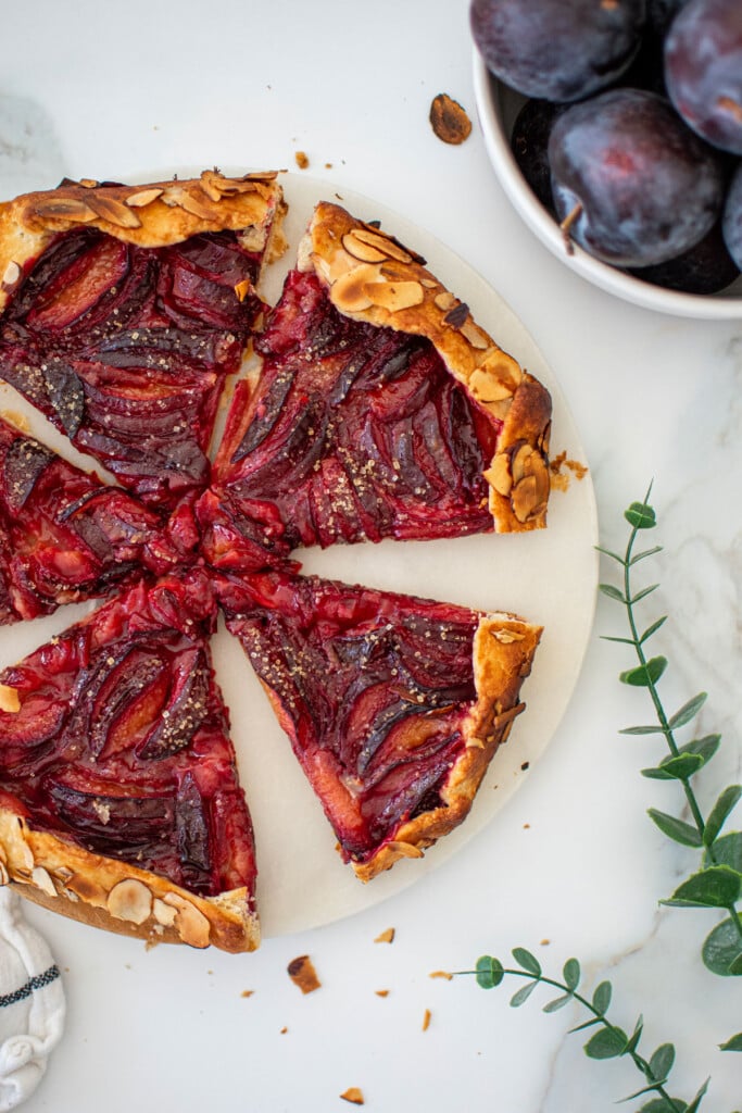 honey almond plum galette cut into slices on a marble plate on a white marble countertop.