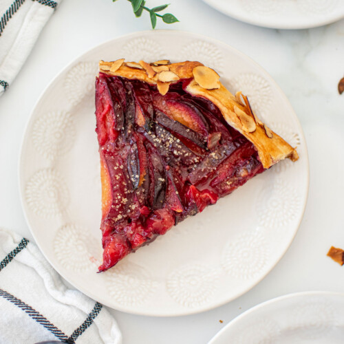 honey almond plum galette slice on a white plate on a white marble countertop.