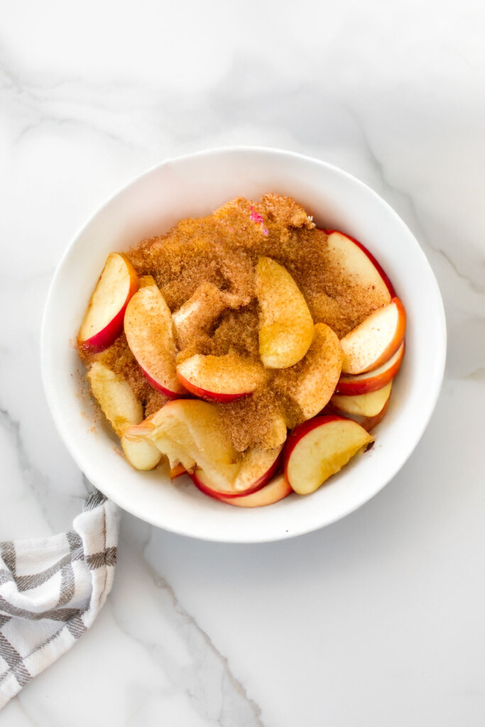 white bowl of apples honey and brown sugar on a white marble counter.