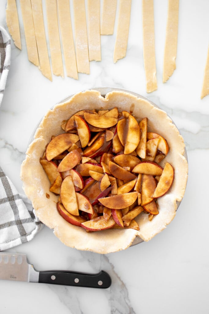 pie pan with crust and apple pie filling on a white marble counter.
