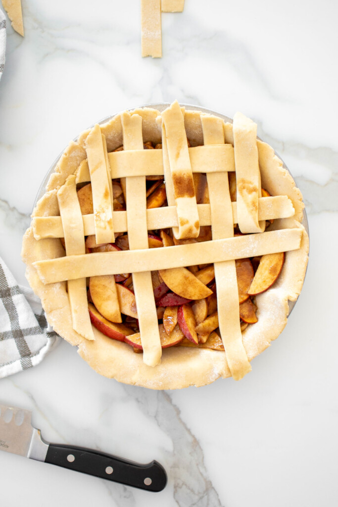 apple pie being latticed with strips of dough on top on a white marble countertop.