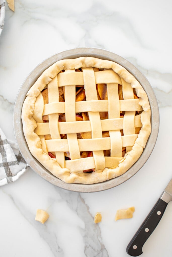 apple pie latticed with strips of dough on top on a white marble countertop.