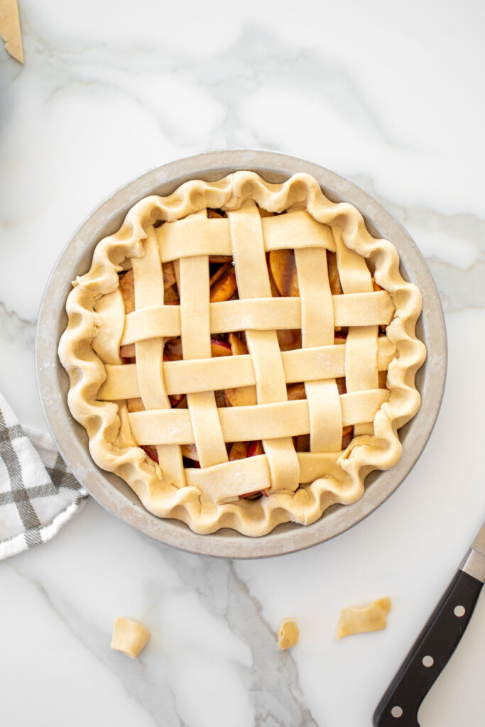 apple pie latticed with strips of dough on top and fluted edges on a white marble countertop.