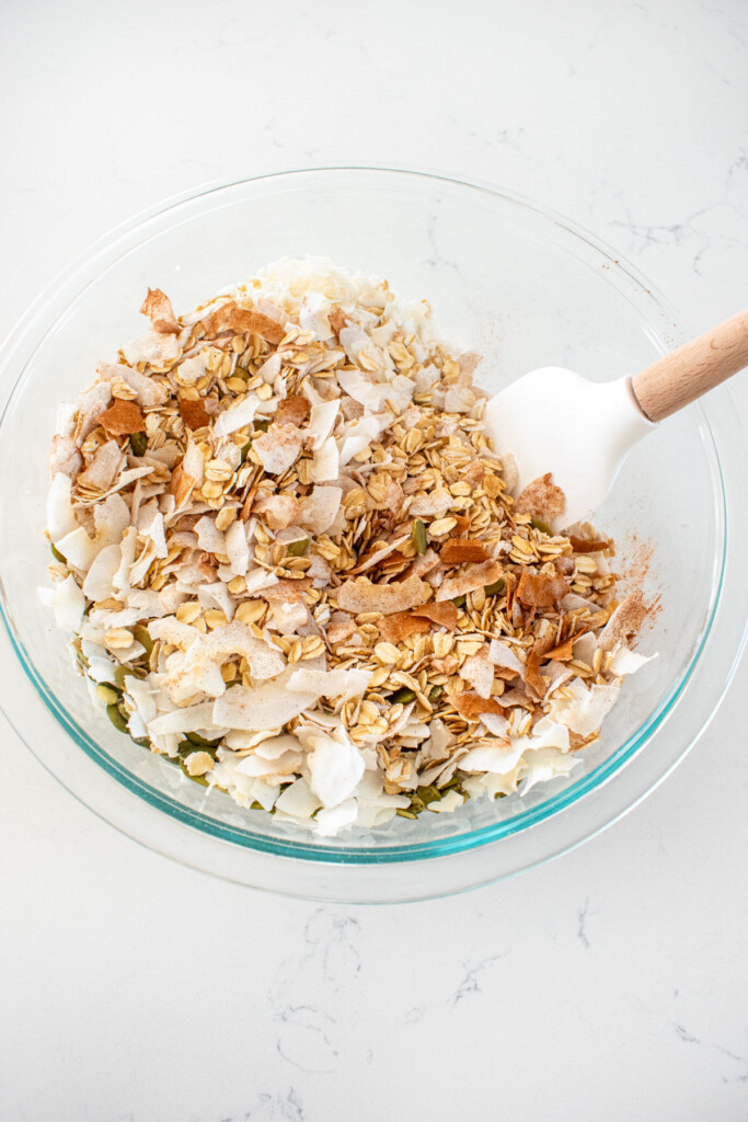 dry ingredients being mixed for maple cinnamon olive oil granola in a glass mixing bowl on a white marble counter.