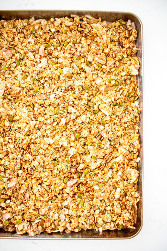 maple cinnamon olive oil granola spread out onto a baking sheet.