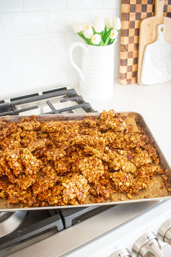 baked maple cinnamon olive oil granola clusters cooling on a baking sheet on top of the oven.
