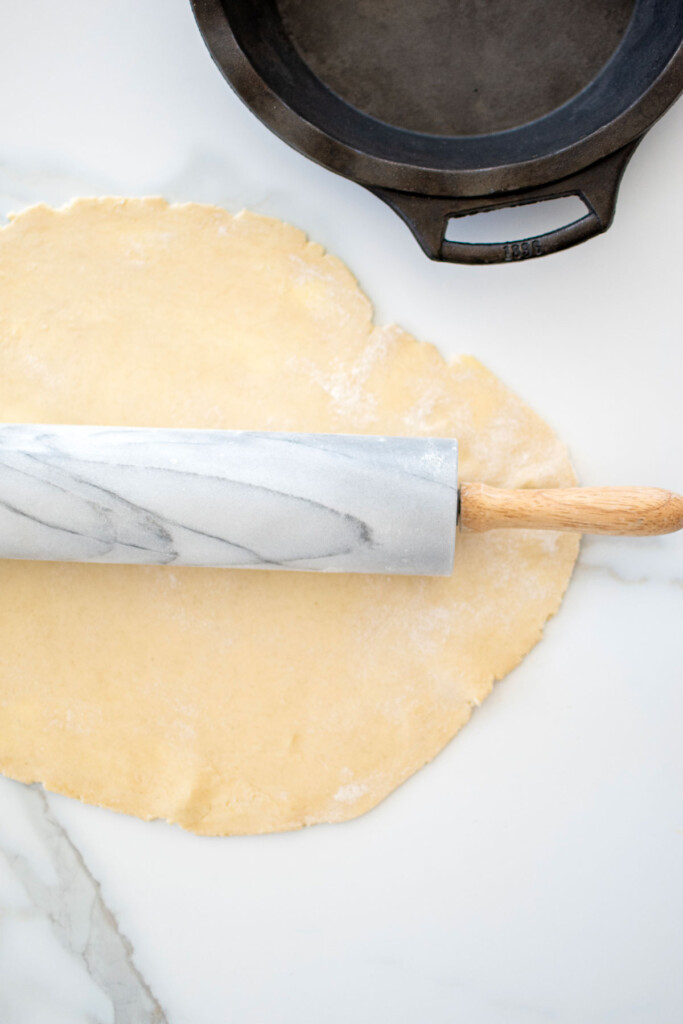 pie crust being rolled out on a marble counter with a marble rolling pin.