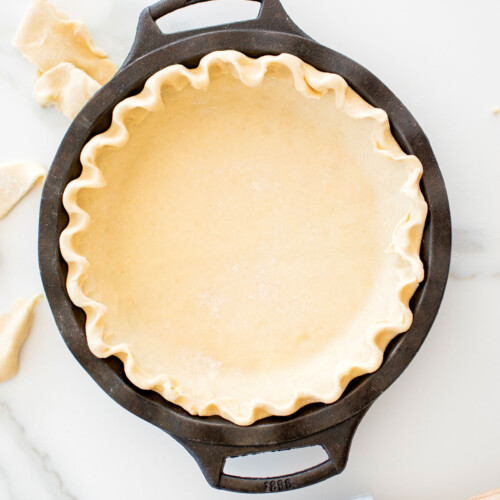 fluted pie crust in a cast iron pie pan on a white marble counter.