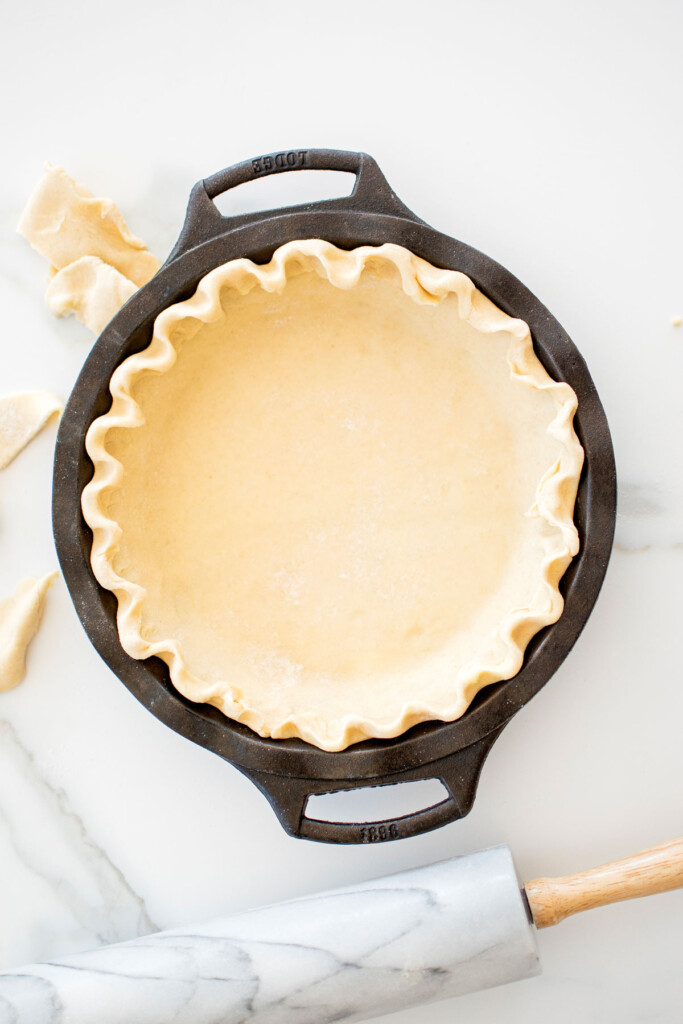 fluted pie crust in a cast iron pie pan on a white marble counter.