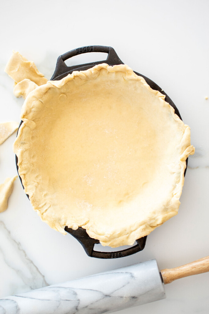 pie crust in a cast iron pie pan on a white marble counter.