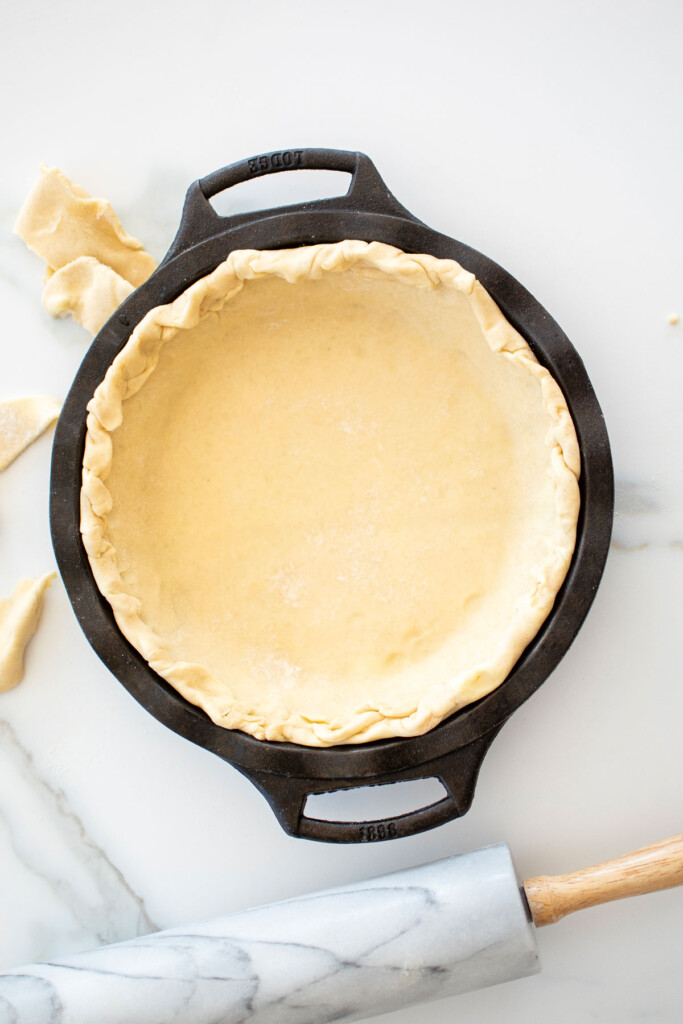 pie crust in a cast iron pie pan on a white marble counter.
