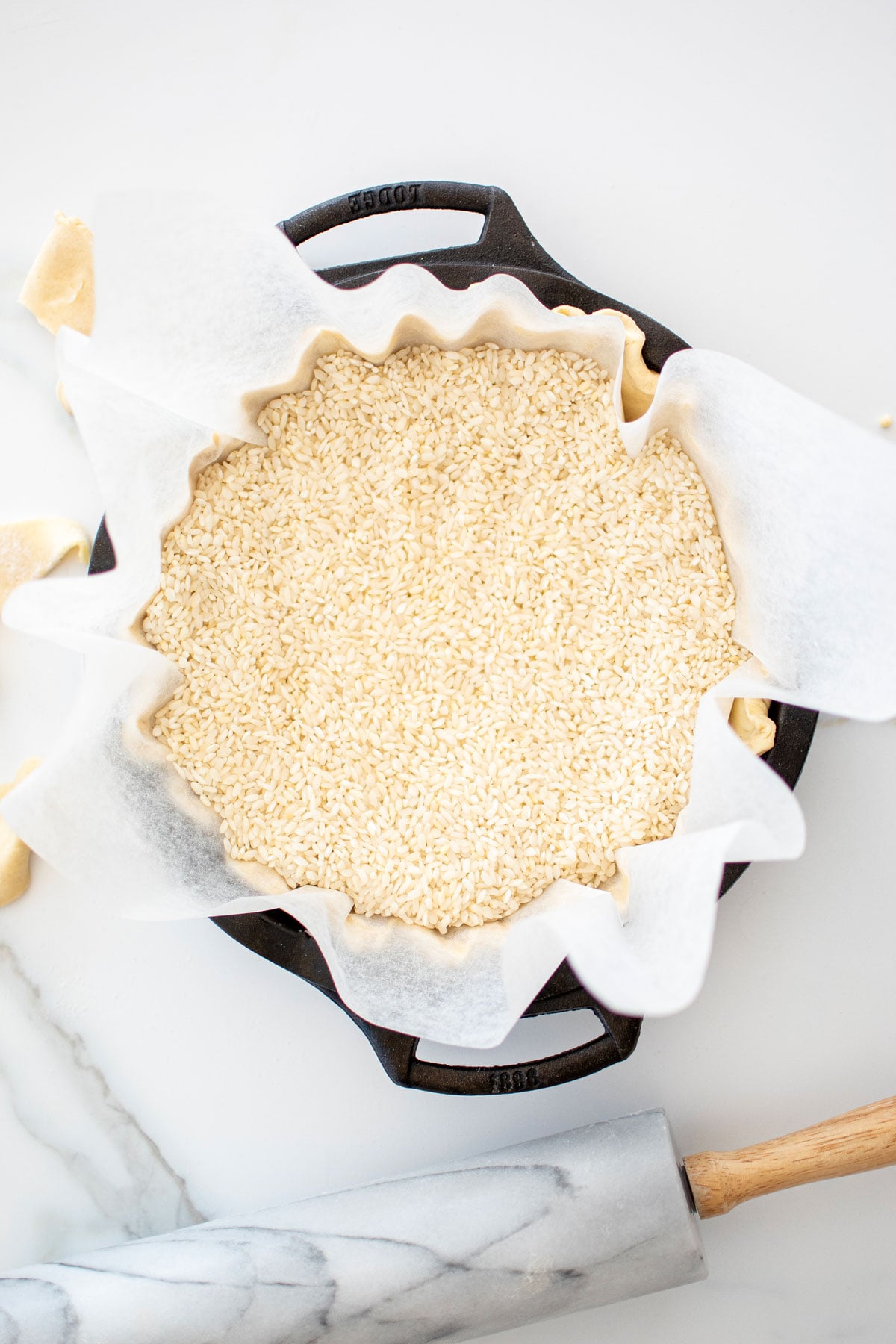 pie crust with parchment paper and rice in a cast iron pie pan on a white marble counter.