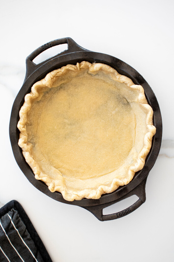 parbaked pie crust in a cast iron pie pan on a white marble counter.