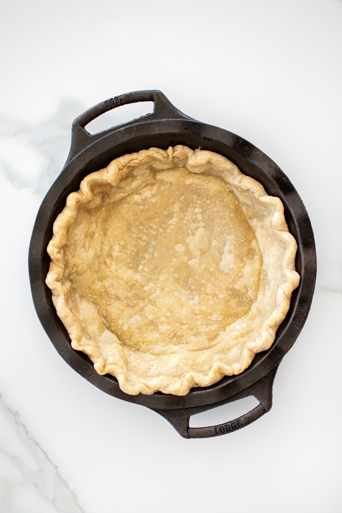parbaked pie crust in a cast iron pie pan on a white marble counter.