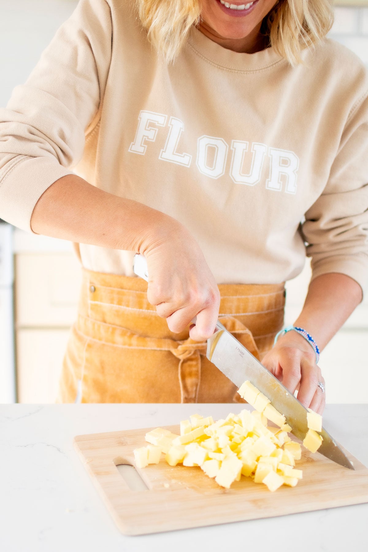woman chopping butter in small pieces on a wood cutting board in the kitchen counter.