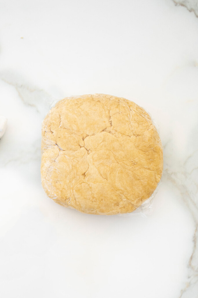 pie dough wrapped in plastic wrap on a white marble counter.