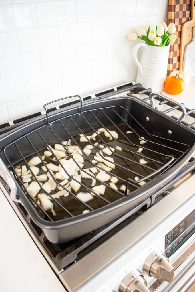 chopped onion and chicken broth in a roasting pan on top of the stovetop.